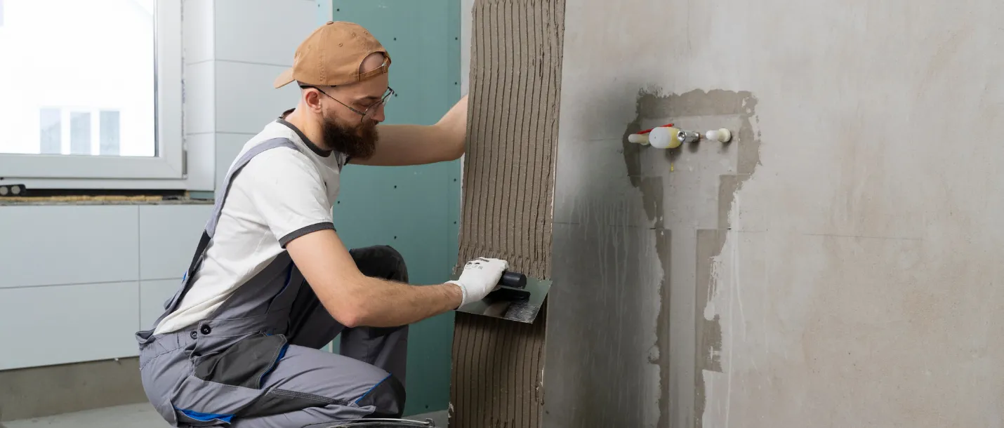 Worker applying wall tiles during bathroom renovation and remodeling process
